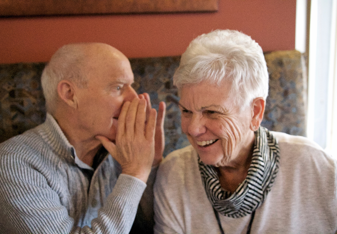 man talking in the ear of a woman struggling from hearing loss